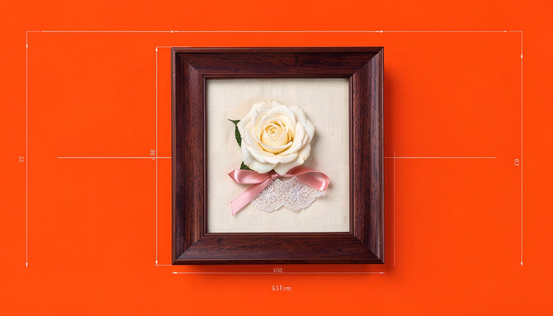 A deep walnut-toned shadowbox frame displaying a pressed ivory rose, a lace garter, and a small satin ribbon against a soft cream linen backing, warm and romantic